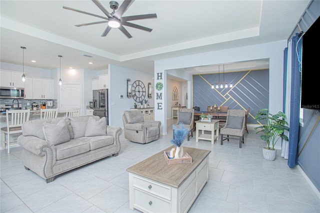 living area featuring visible vents, an accent wall, light tile patterned flooring, baseboards, and ceiling fan with notable chandelier