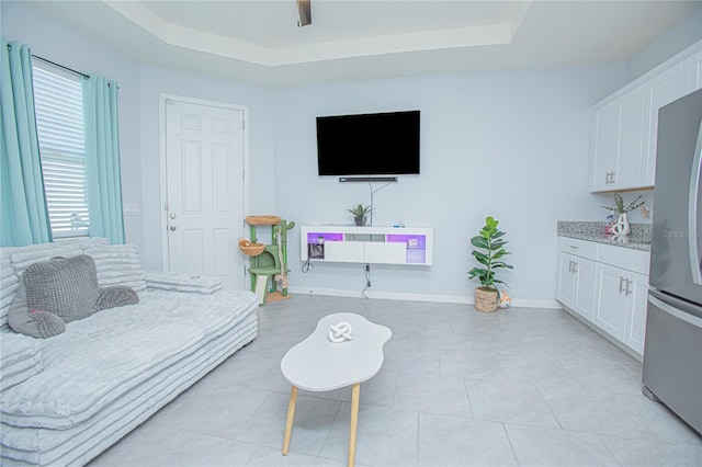 bedroom featuring light tile patterned floors, a ceiling fan, baseboards, freestanding refrigerator, and a tray ceiling