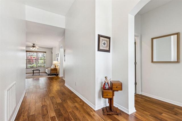 hallway featuring baseboards, visible vents, arched walkways, and wood finished floors