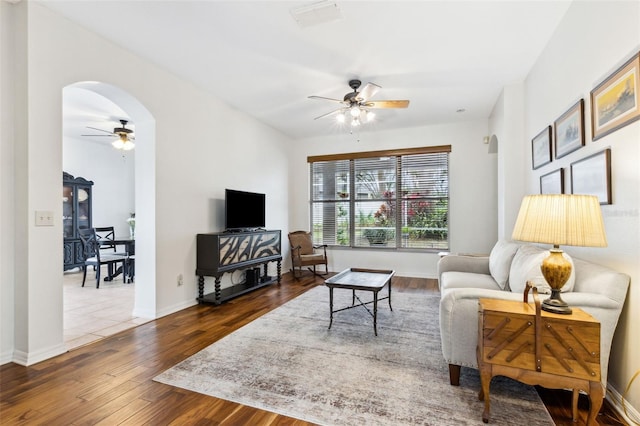 living area with ceiling fan, arched walkways, dark wood finished floors, and baseboards