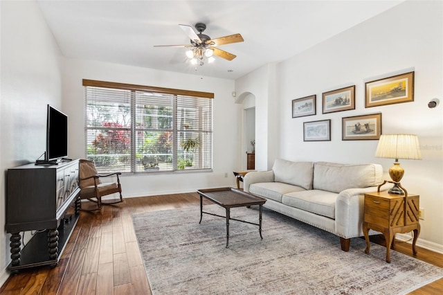 living area featuring arched walkways, ceiling fan, wood finished floors, and baseboards