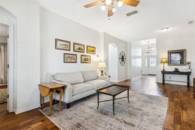 living room featuring dark wood-style floors, arched walkways, visible vents, and baseboards