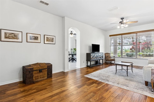 living room with arched walkways, visible vents, dark wood-type flooring, a ceiling fan, and baseboards