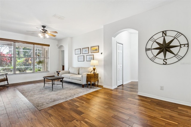 living area featuring arched walkways, visible vents, dark wood-type flooring, ceiling fan, and baseboards