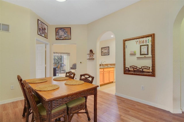 dining area featuring arched walkways, light wood-style flooring, visible vents, and baseboards