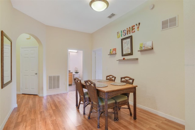 dining area with arched walkways, visible vents, and light wood-style flooring