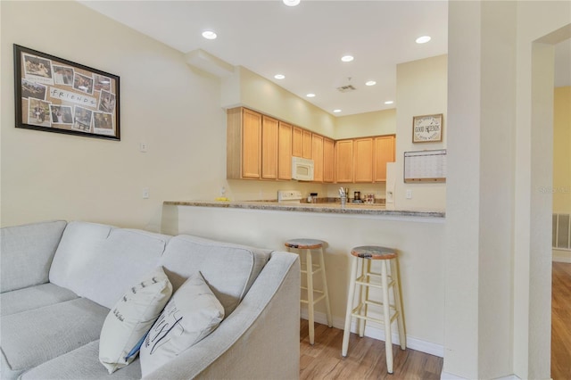 kitchen with white microwave, a breakfast bar area, light wood-style flooring, and recessed lighting