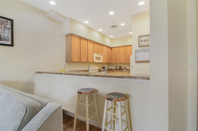 kitchen featuring visible vents, range, white microwave, a breakfast bar area, and wood finished floors