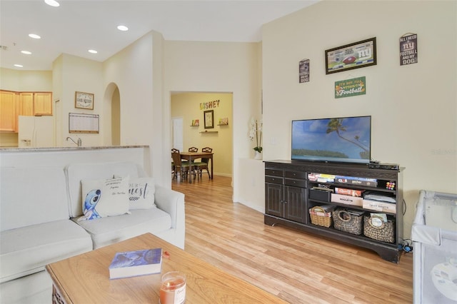 living area featuring light wood-type flooring, baseboards, arched walkways, and recessed lighting