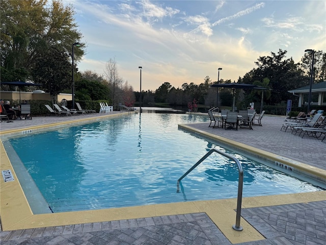 pool at dusk featuring a patio and a community pool