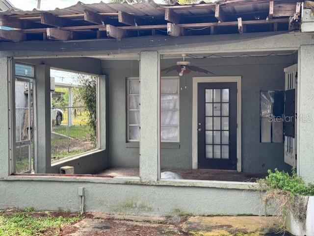 entrance to property with a ceiling fan and stucco siding