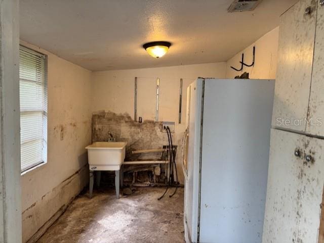 kitchen with freestanding refrigerator, visible vents, a sink, and unfinished concrete flooring