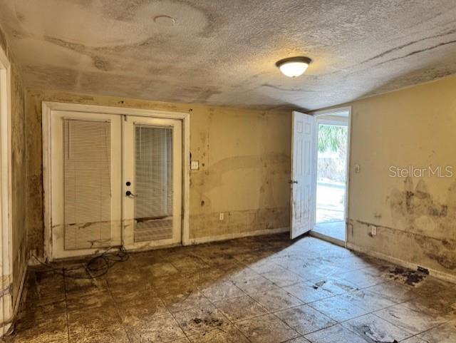 unfurnished room with french doors, a textured ceiling, and tile patterned floors