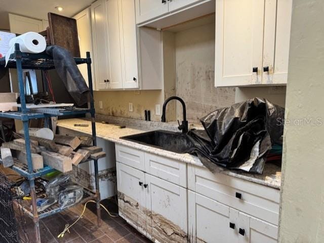 kitchen with a sink, white cabinetry, and light stone countertops