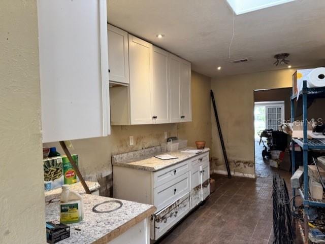 kitchen featuring visible vents, a skylight, white cabinetry, and light stone countertops