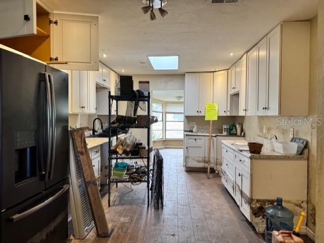 kitchen featuring a skylight, white cabinetry, black refrigerator with ice dispenser, and light countertops