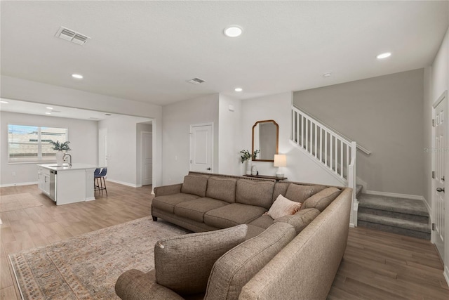 living room with baseboards, visible vents, stairway, and light wood finished floors