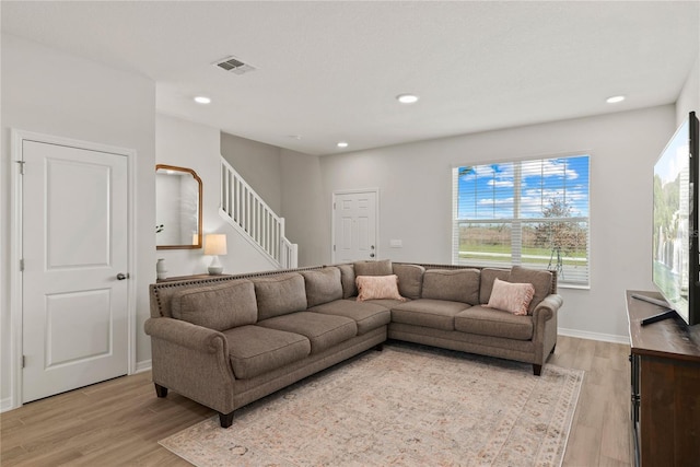 living area with stairway, light wood-style flooring, visible vents, and baseboards