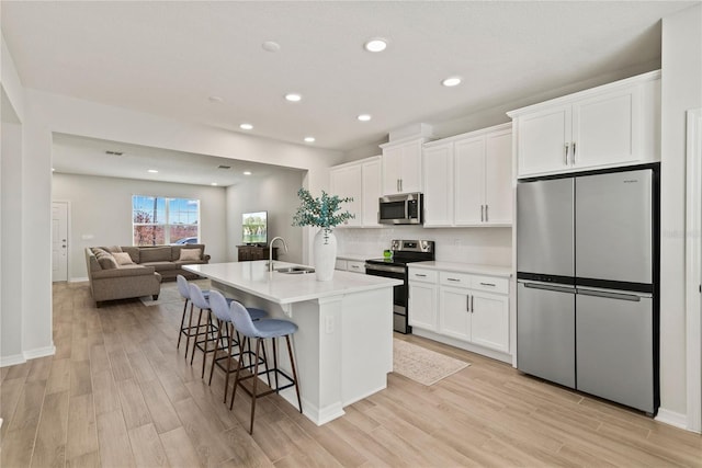 kitchen with stainless steel appliances, a sink, white cabinetry, light countertops, and a center island with sink