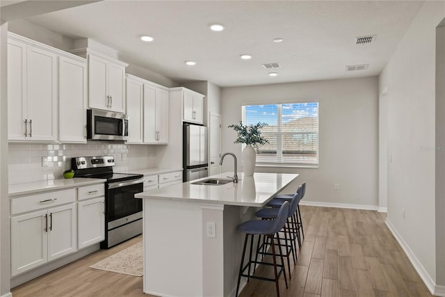 kitchen with light countertops, appliances with stainless steel finishes, white cabinets, a sink, and an island with sink