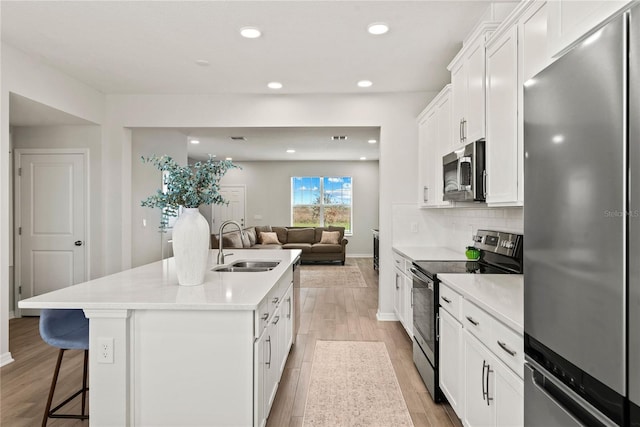 kitchen with appliances with stainless steel finishes, light countertops, open floor plan, and a kitchen island with sink