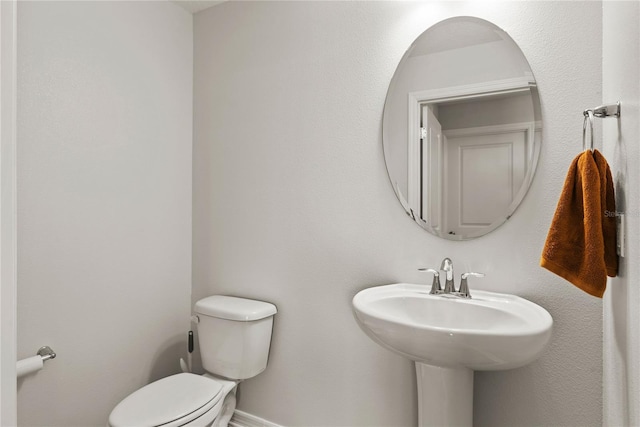 half bath with baseboards, a sink, and toilet