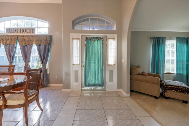 entryway featuring baseboards, a high ceiling, arched walkways, and light tile patterned flooring