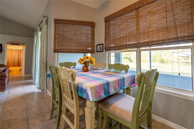 dining space with arched walkways, light tile patterned flooring, lofted ceiling, and baseboards