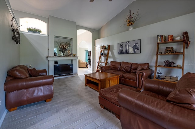 living area with high vaulted ceiling, arched walkways, wood finished floors, and a glass covered fireplace