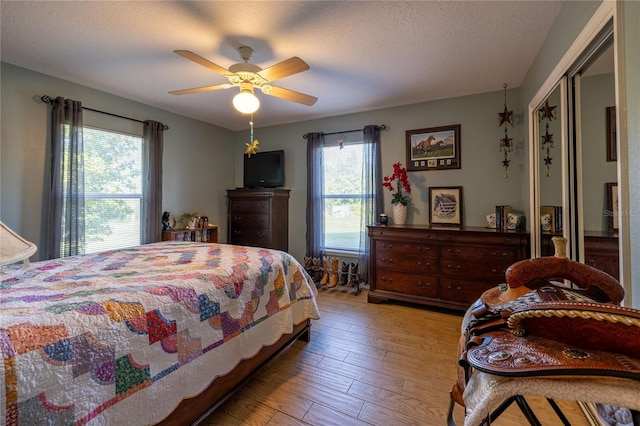 bedroom with light wood-style floors, a textured ceiling, and a ceiling fan