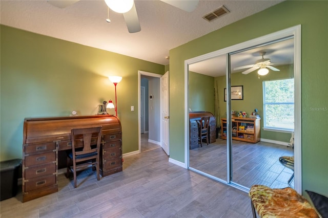 office space featuring ceiling fan, a textured ceiling, wood finished floors, visible vents, and baseboards