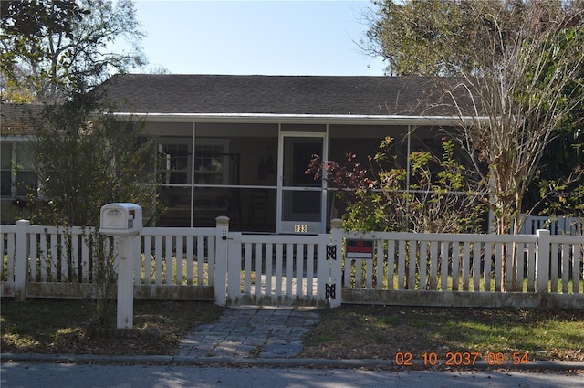 view of front of home with a sunroom, roof with shingles, a fenced front yard, and a gate