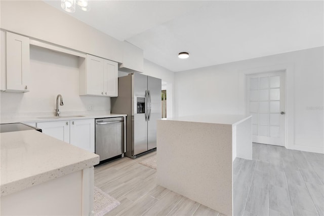 kitchen with appliances with stainless steel finishes, wood tiled floor, white cabinetry, a sink, and a kitchen island