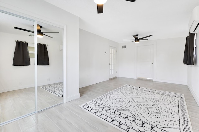 unfurnished bedroom featuring light wood-style floors, visible vents, a ceiling fan, and a wall mounted AC