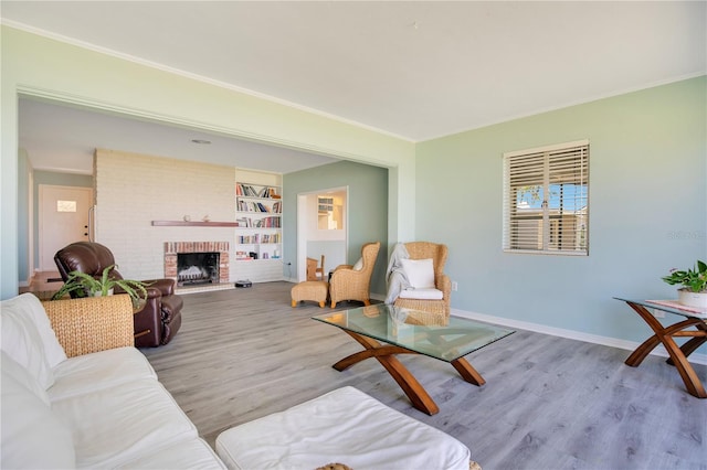 living room featuring a brick fireplace, crown molding, baseboards, and wood finished floors