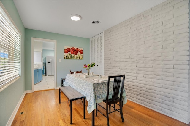 dining space featuring brick wall, light wood-style flooring, visible vents, and baseboards