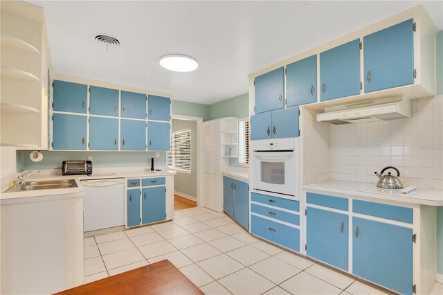 kitchen featuring open shelves, a sink, blue cabinets, white appliances, and under cabinet range hood