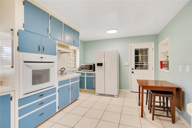 kitchen featuring white appliances, baseboards, light countertops, blue cabinetry, and light tile patterned flooring