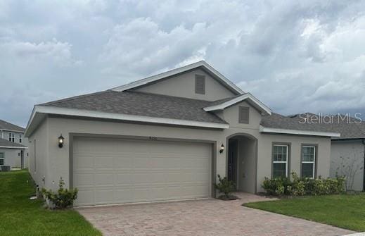 ranch-style home featuring an attached garage, a front lawn, decorative driveway, and stucco siding