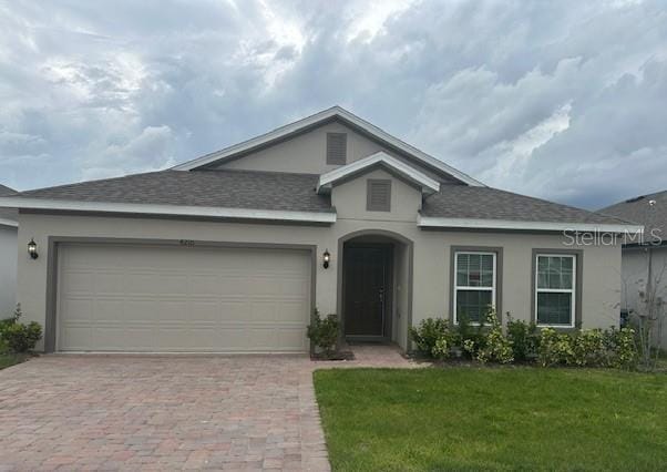 ranch-style house featuring a garage, stucco siding, roof with shingles, decorative driveway, and a front yard