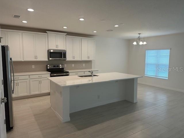 kitchen with stainless steel appliances, pendant lighting, light countertops, and a center island with sink