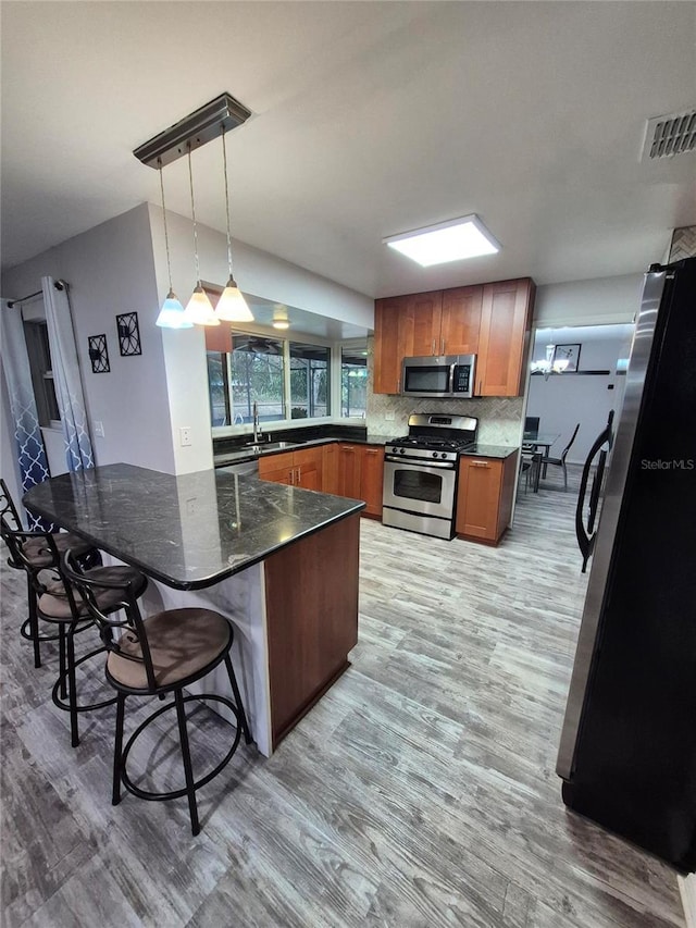 kitchen with visible vents, a breakfast bar area, appliances with stainless steel finishes, brown cabinetry, and a sink