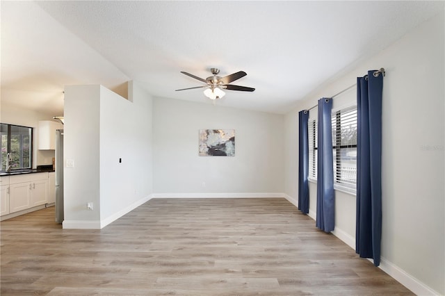 empty room with a sink, a ceiling fan, baseboards, vaulted ceiling, and light wood-type flooring