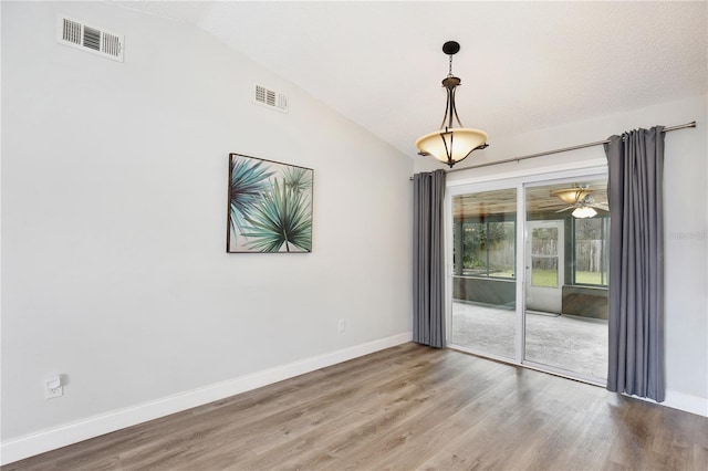 spare room with lofted ceiling, wood finished floors, visible vents, and baseboards