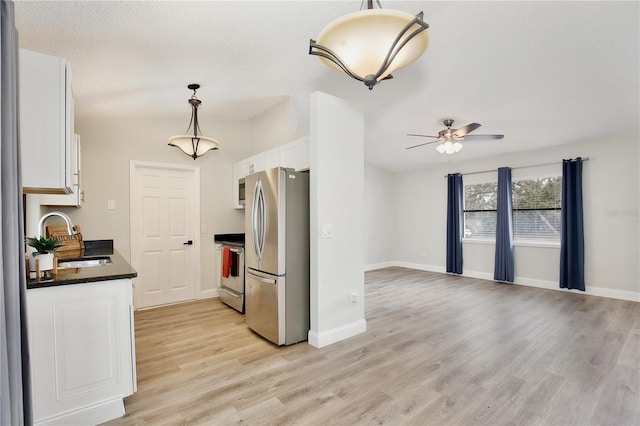 kitchen featuring dark countertops, appliances with stainless steel finishes, light wood-style floors, white cabinets, and a sink