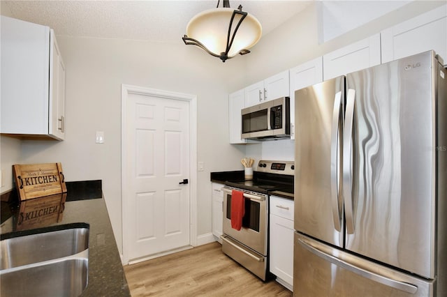 kitchen featuring stainless steel appliances, white cabinetry, a sink, a textured ceiling, and light wood-type flooring