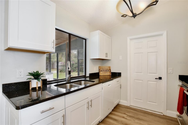 kitchen featuring light wood-style flooring, white cabinets, a sink, dark stone countertops, and dishwasher