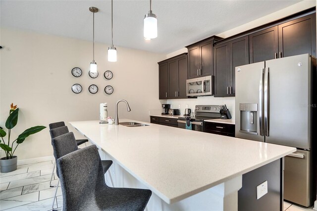 kitchen featuring hanging light fixtures, appliances with stainless steel finishes, a sink, and a kitchen island with sink