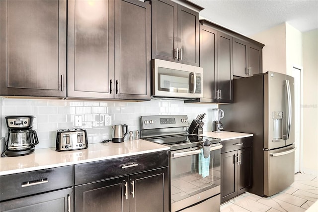 kitchen with marble finish floor, light countertops, appliances with stainless steel finishes, dark brown cabinets, and decorative backsplash