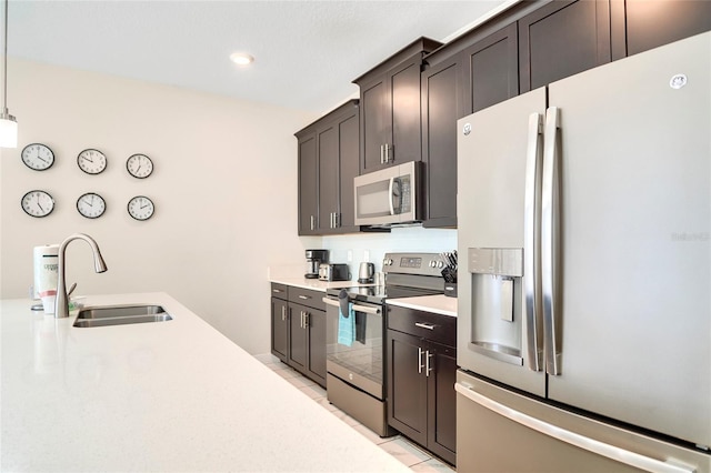 kitchen with a sink, light countertops, appliances with stainless steel finishes, hanging light fixtures, and dark brown cabinets